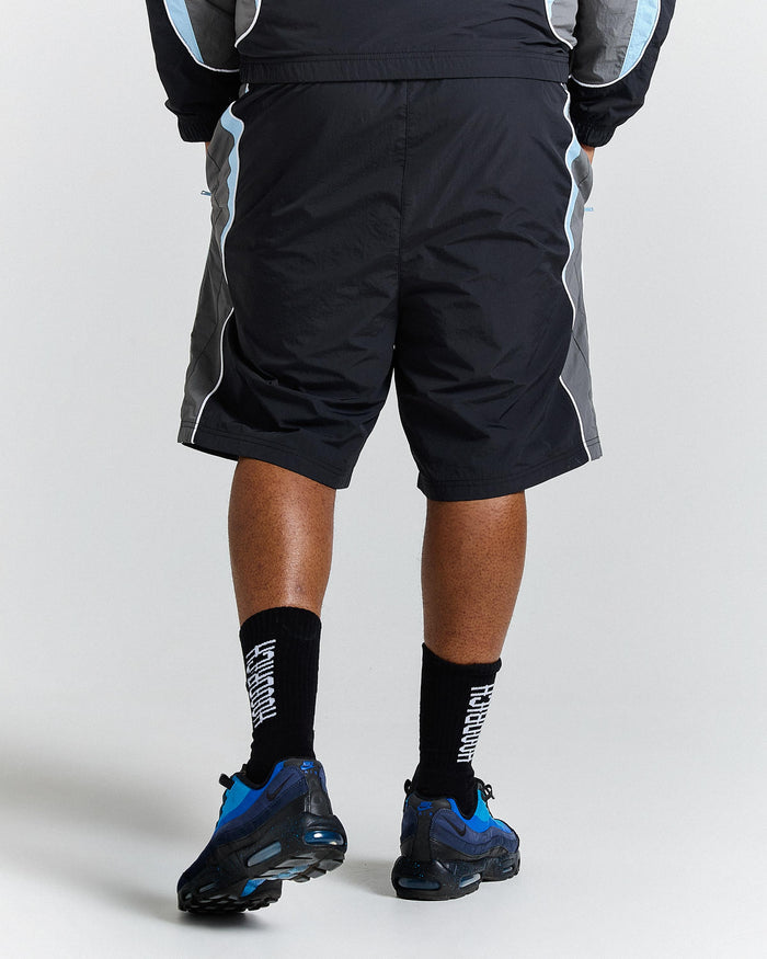Person wearing black athletic shorts, black socks with white text, and blue athletic shoes on a light grey background