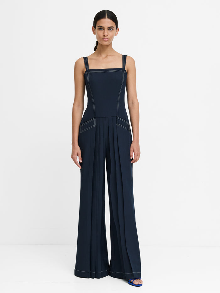 Woman wearing a navy jumpsuit with straps and white stitching