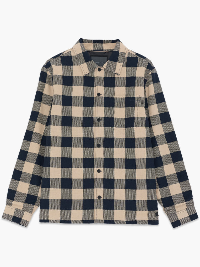 A man wearing a sandy navy check Over-shirt with long sleeves, a pointed collar, a button down fastening, a chest patch pocket and a regular fit.