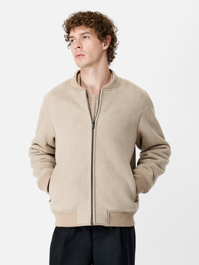 A man wearing a sand bomber jacket with long sleeves, a crew neck and a zip down front.