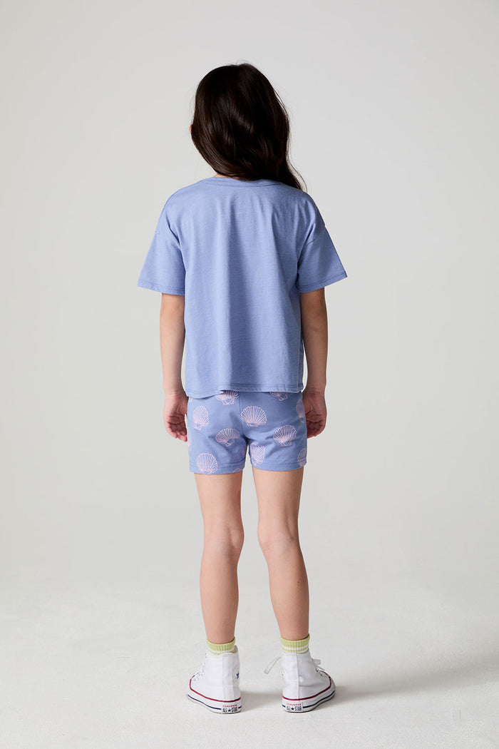 Full body back view of a girl wearing the Chaser Seashell Dreams Allover Shorts on a neutral background