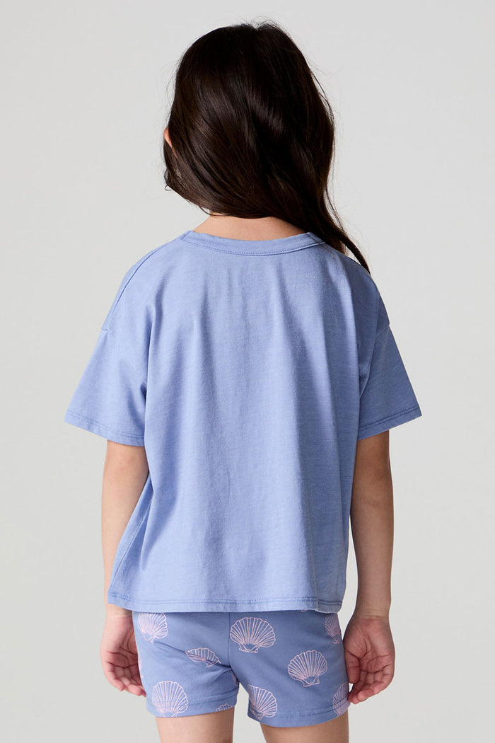 Back view of a girl wearing the Chaser Seashell Dreams Tee on a neutral background with arms at sides