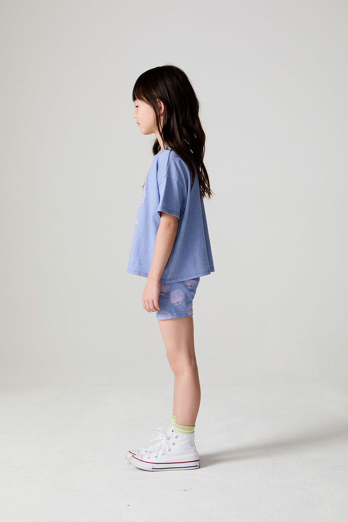 Full body side view of a girl wearing the Chaser Seashell Dreams Tee on a neutral background