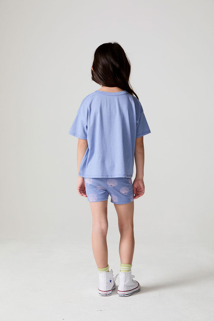 Full body back view of a girl wearing the Chaser Seashell Dreams Tee and shorts on a neutral background