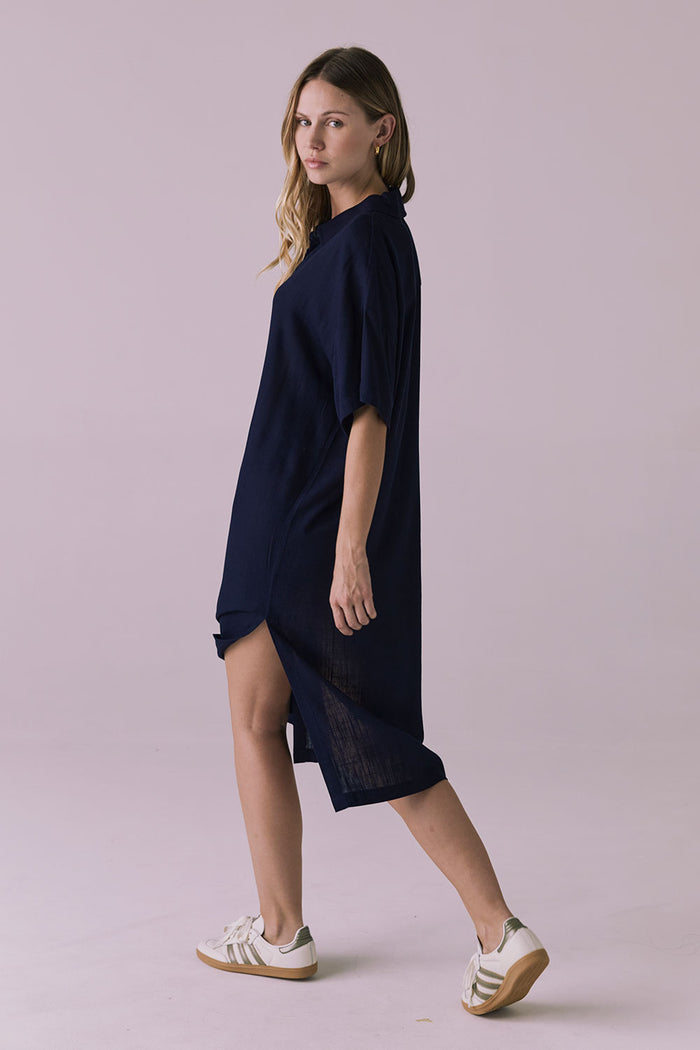 Full body side walking view of the Chaser Seaside Navy Button Up Dress showing the loose sleeve shape and curved hem