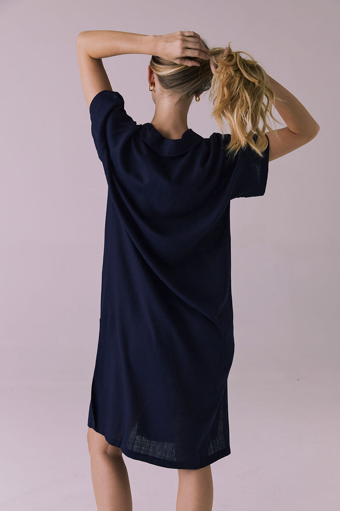 Full body back view of the Chaser Seaside Navy Button Up Dress with relaxed shoulders and side vent hem