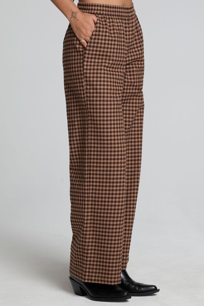 Side view of a woman wearing the Chaser Seren Choco Check Pants on a neutral background with hands in pockets
