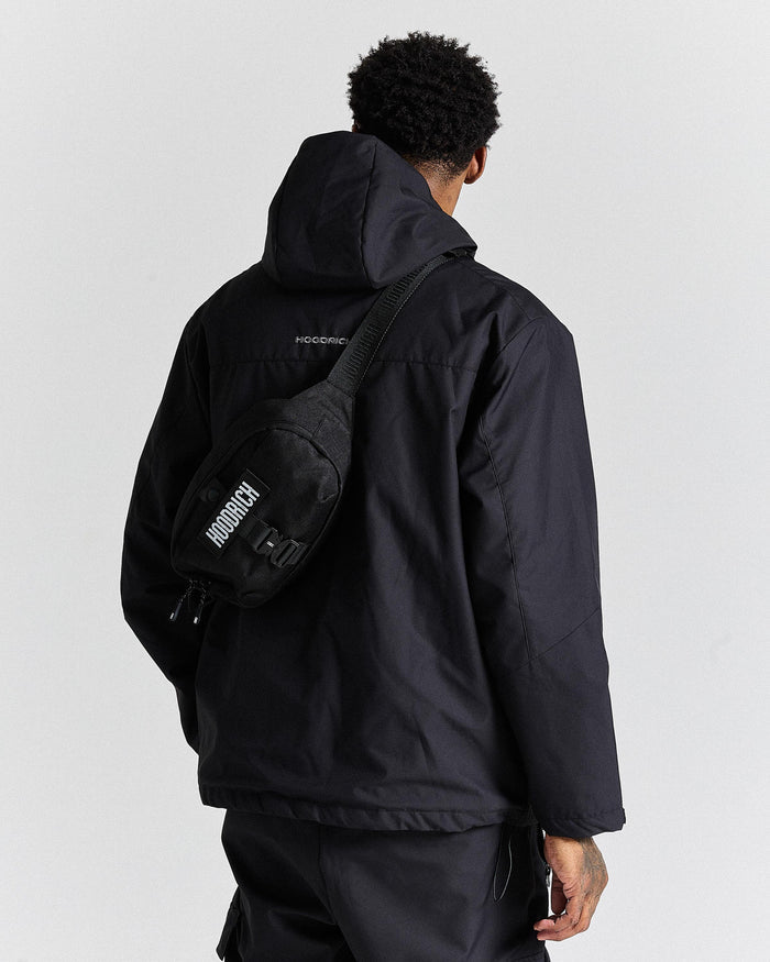 Person wearing a black jacket and carrying a black bag with 'Hoodrich' branding on a light gray background