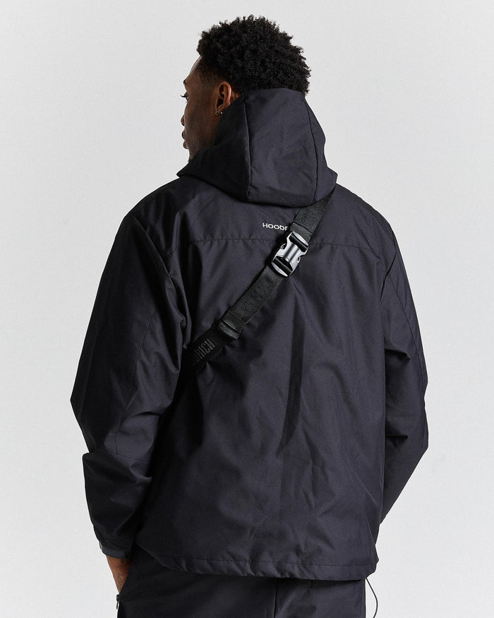 Person wearing a black jacket with a visible brand logo on a light gray background