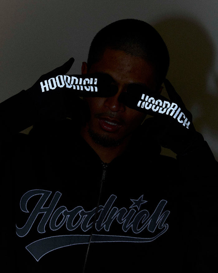 Person wearing a black hoodie with 'Hoodrich' branding, holding reflective wristbands.