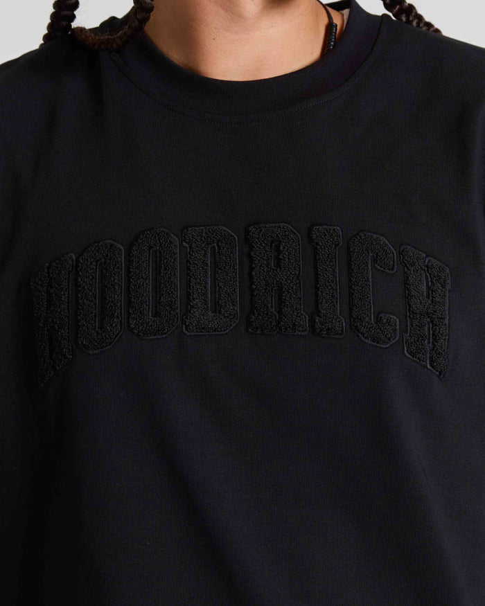 Close-up of a person wearing a black crewneck sweatshirt with 'HOODRICH' embroidered in black across the chest.