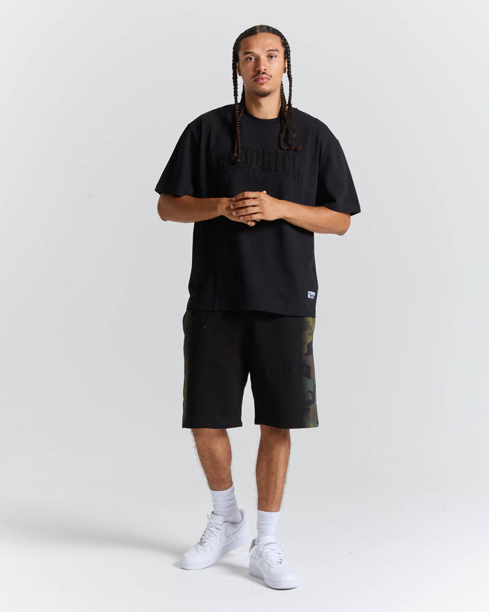 A man modeling a black short-sleeve t-shirt and matching black shorts with subtle camouflage details on the side, paired with white socks and white sneakers, against a light gray studio background.