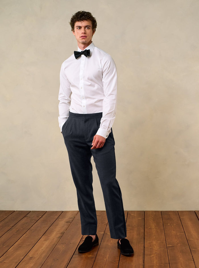 Man in shadow black linen tuxedo pants, white shirt, and black bow tie, front full-body view