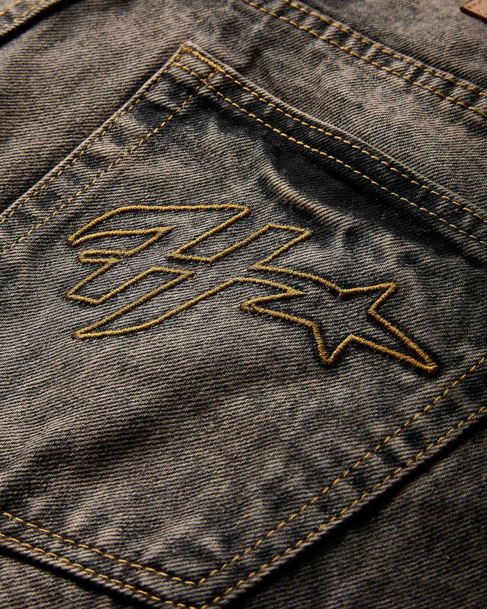 Close-up of the Hoodrich logo embroidered on the pocket of the regular fit black rust washed denim jorts.