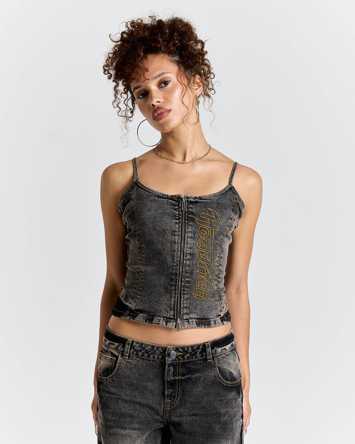 Model wearing a fitted black denim corset top with a zip front and yellow Hoodrich logo embroidery.