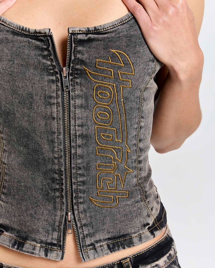 Close-up of the zip front and yellow Hoodrich logo embroidery on a model wearing a fitted black denim corset top.