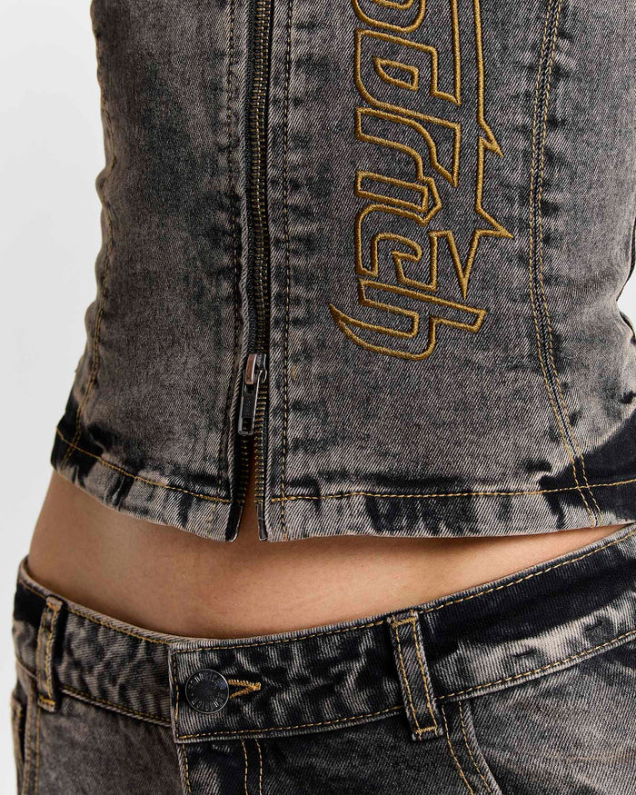 Close-up of the zip hem and yellow Hoodrich logo embroidery on a model wearing a fitted black denim corset top.