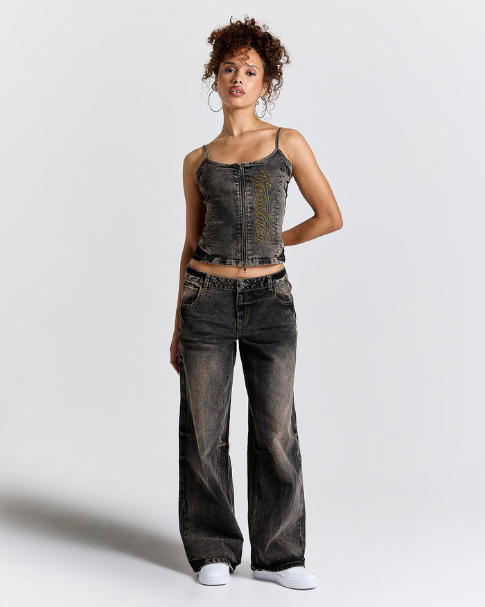 Female model wearing distressed denim corset tank top with wide-leg, rust-coloured wash jeans.