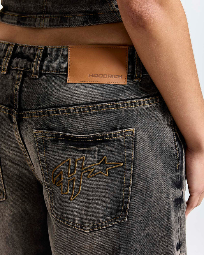 Close-up of a person wearing dark jeans with a brand logo on the pocket and a brown leather patch on the waistband.