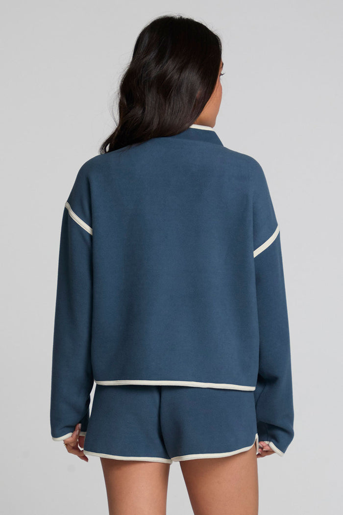 Back view of a woman wearing the Chaser Sharun Dark Denim Jacket and matching shorts on a neutral background