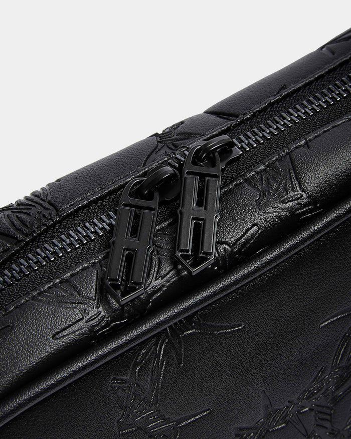 Close-up of a black leather bag with floral embossing and zipper details on a light gray background.