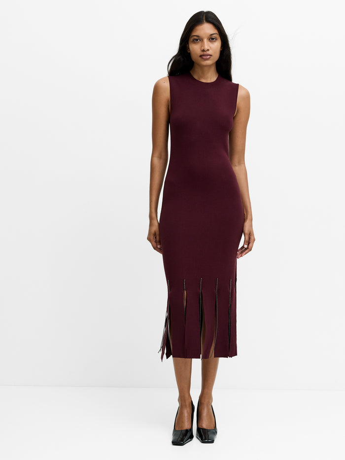 A woman wearing a fitted knit midi dress with a crew neckline, a beaded fringe hem and a midi length.