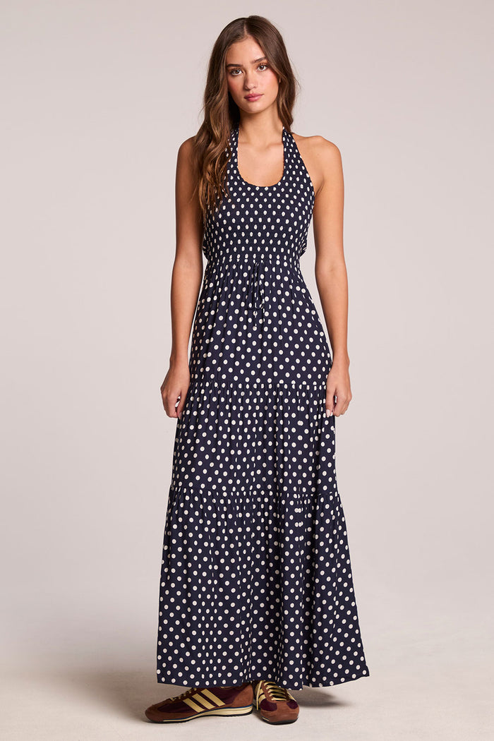 Front view of a woman wearing the Chaser  Siren Navy Spot Maxi Dress  and sneakers on a neutral background