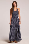 Front view of a woman wearing the Chaser  Siren Navy Spot Maxi Dress  and sneakers on a neutral background