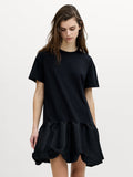 A woman wearing a black dropped shoulder short sleeve T-shirt dress, with a crew neck and peplum hem.