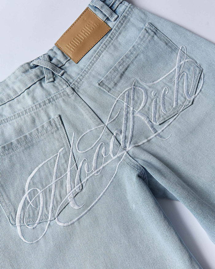 Light blue jeans with 'Hoodrich' embroidery on a white background