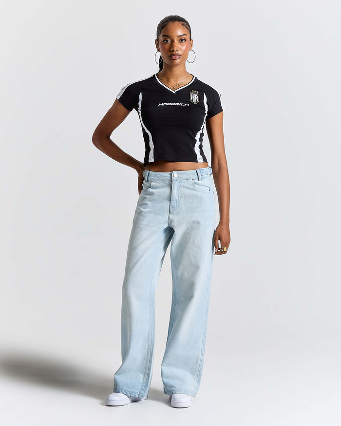 Woman wearing a black and white crop top and light blue jeans on a plain background