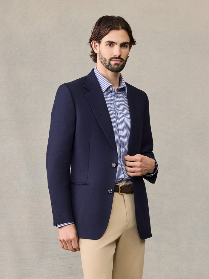 Man in navy sportcoat, striped shirt, and tan trousers, cropped waist-up view