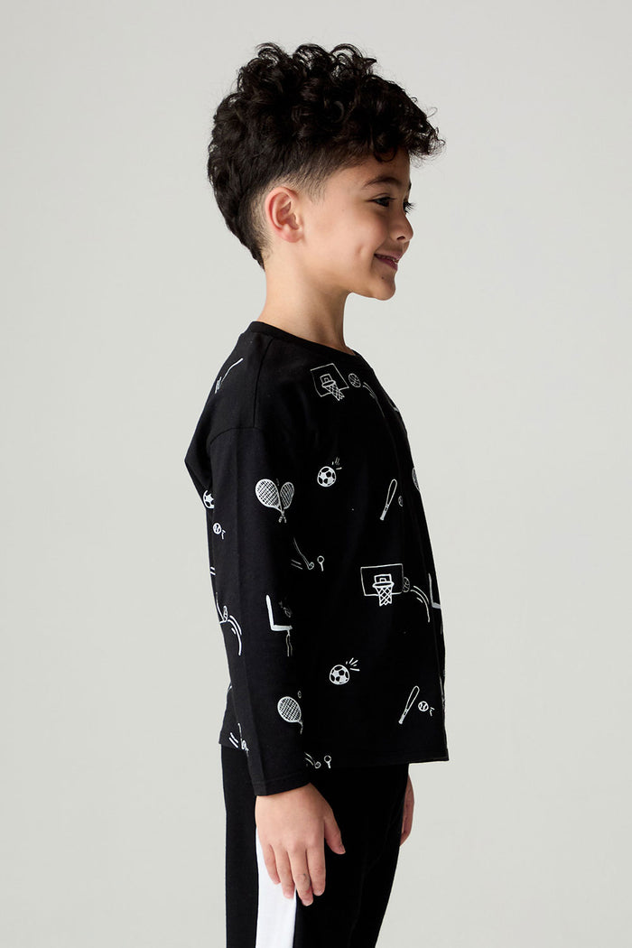 Side view of a boy wearing the Chaser Sports All Over Boys Tee on a neutral background with hands at sides and pants