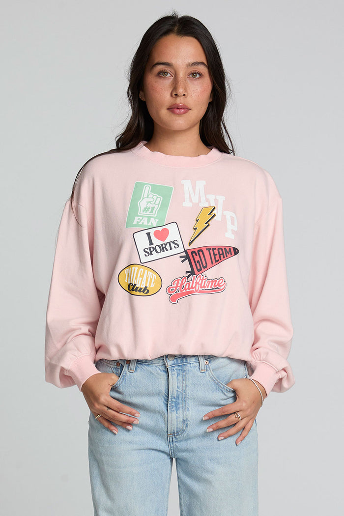 Front view of a woman wearing the Chaser Sporty Patches Long Sleeve Top and blue jeans on a neutral background with hands in pockets