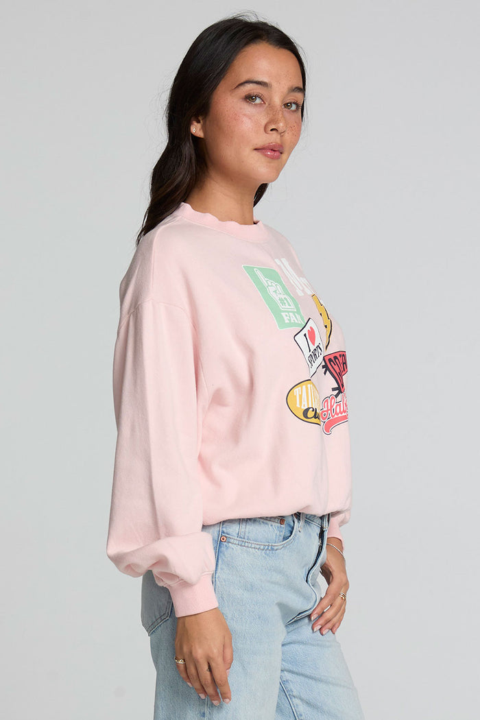 Side view of a woman wearing the Chaser Sporty Patches Long Sleeve Top and blue jeans on a neutral background