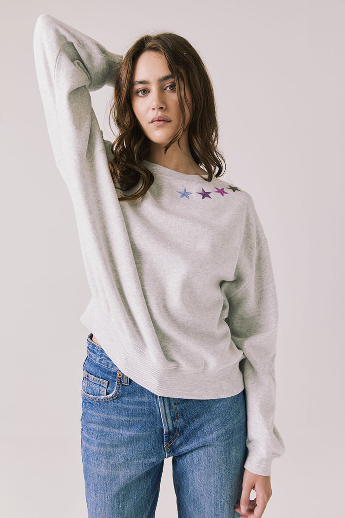 Front view of woman wearing Chaser’s Star Chainstitch Light Grey Long Sleeve with embroidered stars on a plain background