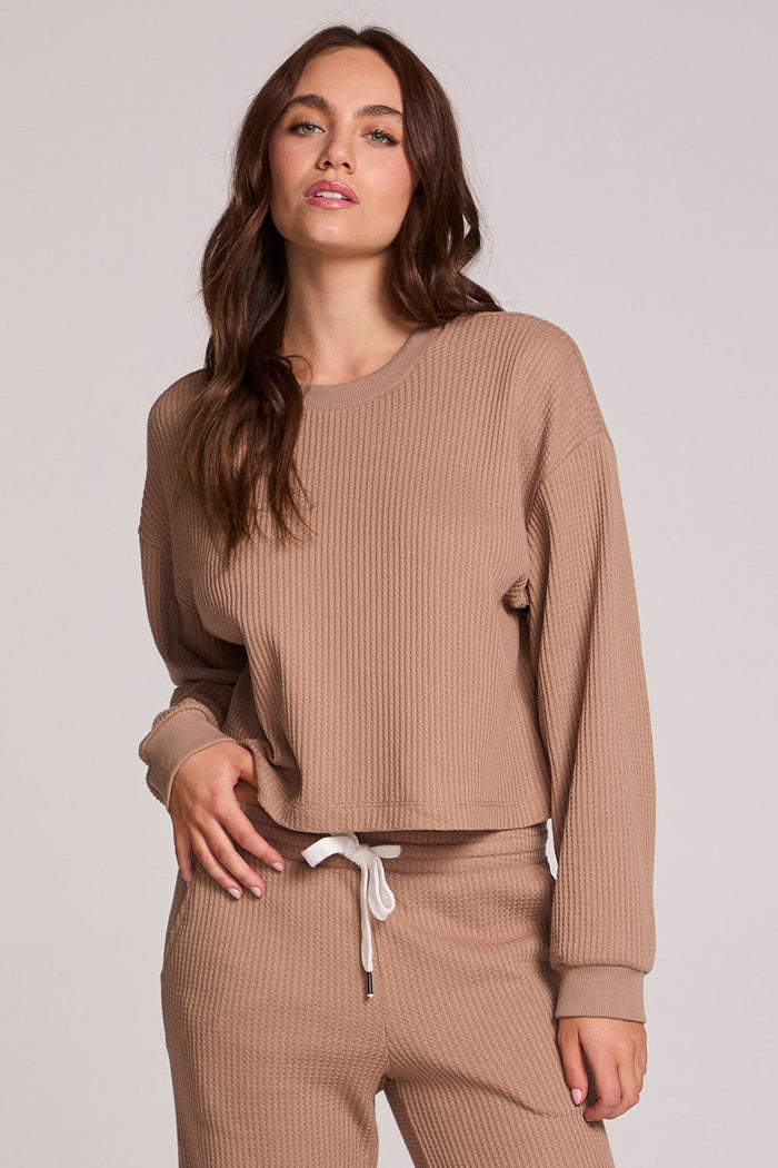 Front view of a woman wearing the Chaser Suzzans Camel Cropped Sweatshirt and matching pants on a neutral background with one hand on waistband