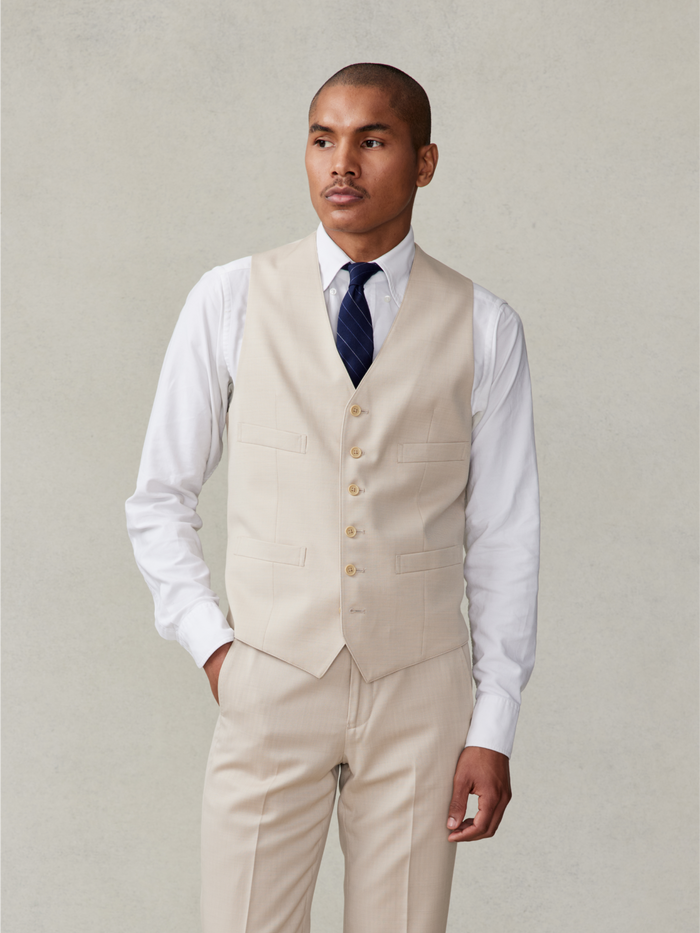 Man in tan suit vest, white shirt, and navy tie, front view, waist-up