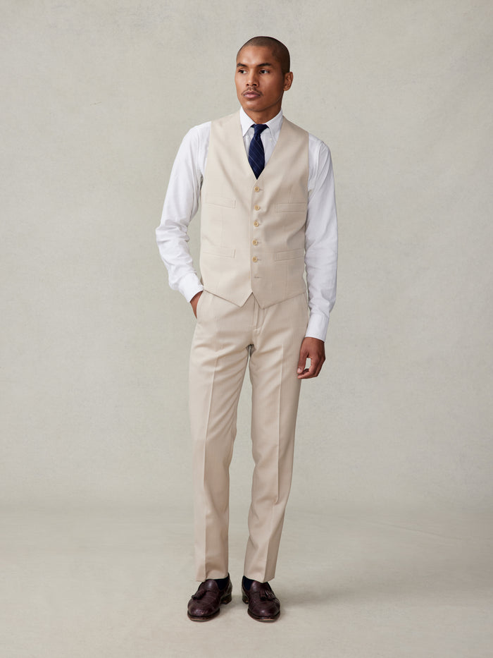 Man in tan suit vest and trousers, white shirt, navy tie, front full-body view