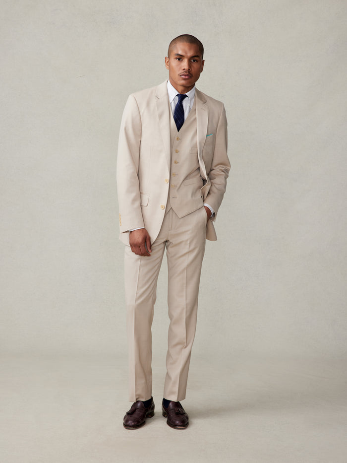 Man in tan three-piece suit with vest, white shirt, and navy tie, front full-body view