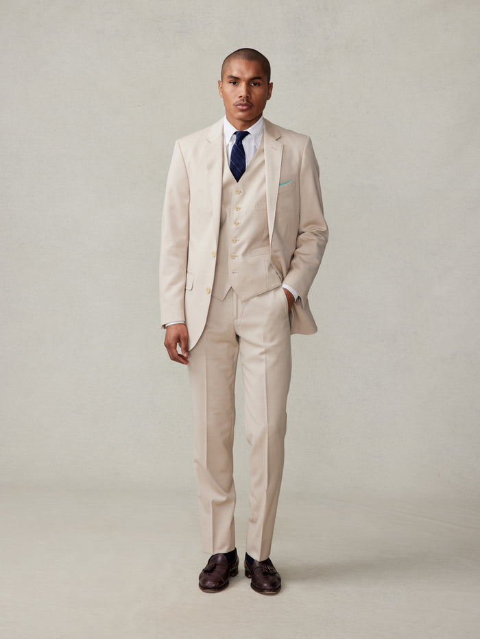 Man in tan three-piece suit, white shirt, and navy tie, front full-body view