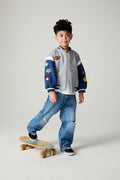 Front view of a boy wearing the Chaser Team Spirit Boys Jacket on a neutral background with jeans and white shirt riding a skateboard