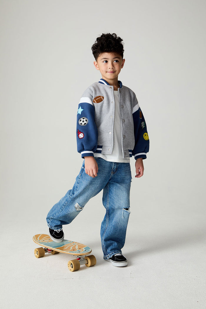Front view of a boy wearing the Chaser Team Spirit Boys Jacket on a neutral background with jeans and white shirt riding a skateboard