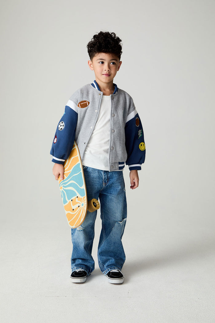 Front view of a boy wearing the Chaser Team Spirit Boys Jacket on a neutral background with jeans and white shirt holding a skateboard under one arm