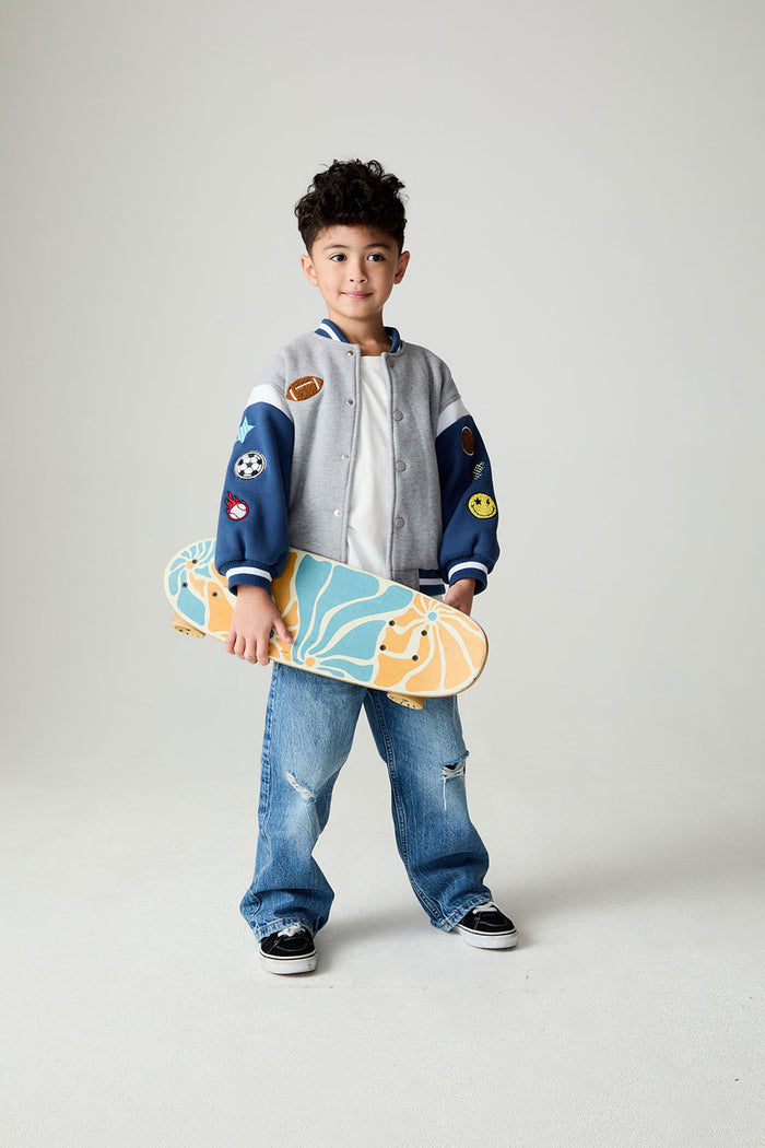 Front view of a boy wearing the Chaser Team Spirit Boys Jacket on a neutral background with jeans and white shirt holding a skateboard