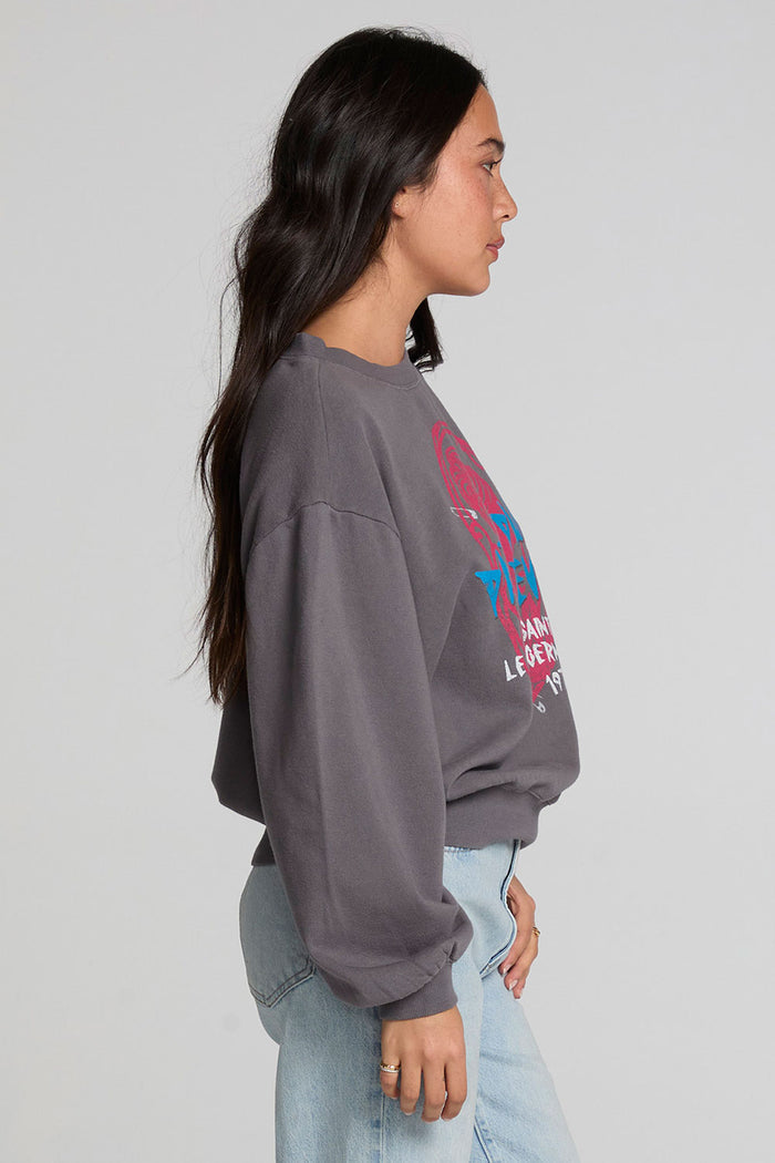Side view of a woman wearing the Chaser The Paris Punk Graphic Sweatshirt and jeans on a neutral background