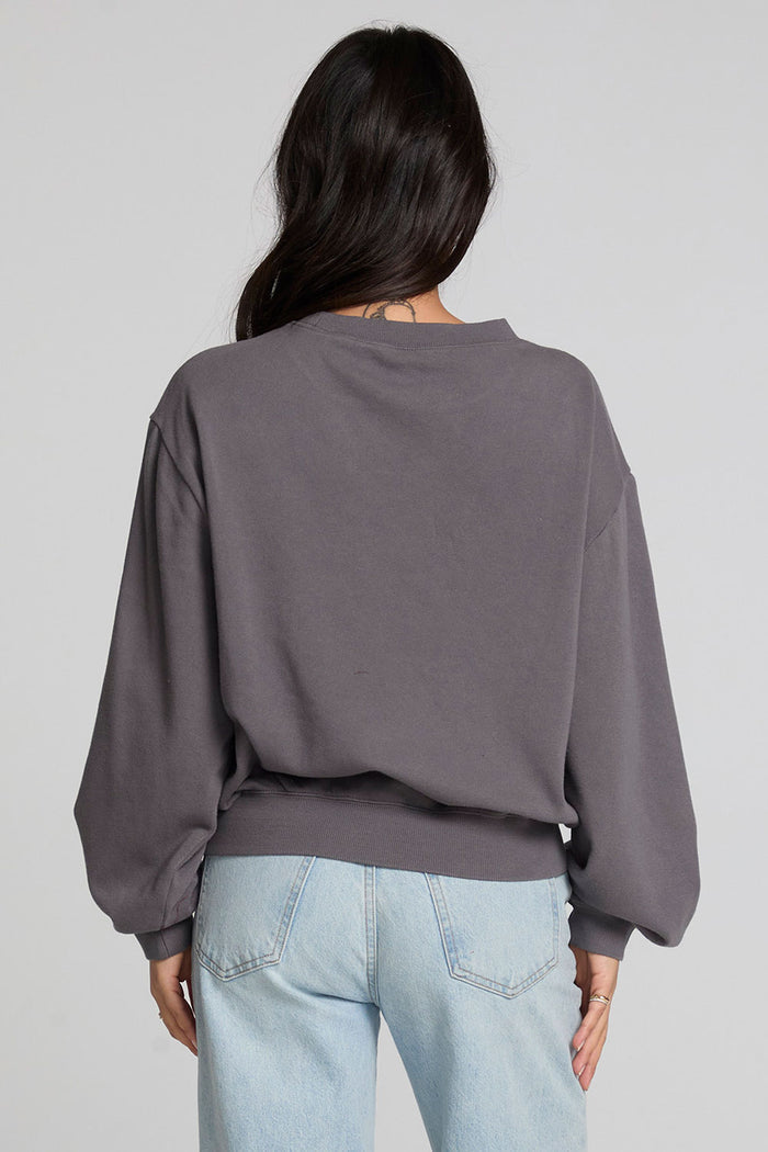 Back view of a woman wearing the Chaser The Paris Punk Graphic Sweatshirt and jeans on a neutral background with arms lowered