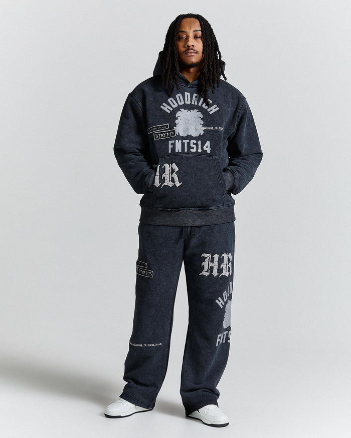 Person wearing a dark gray hoodie and pants with branding on a light gray background