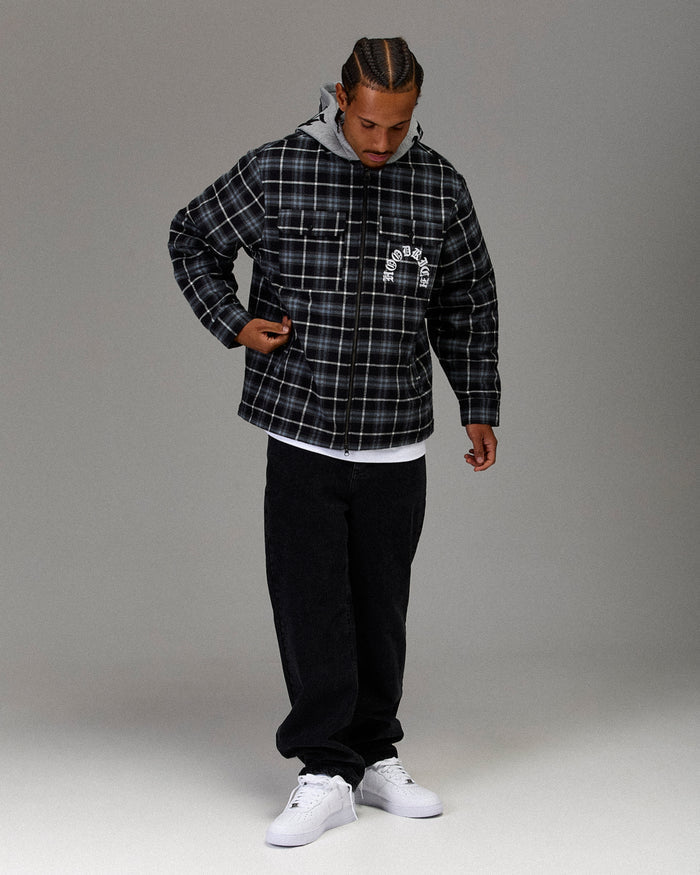 Person wearing a black and gray plaid jacket with a brand logo on a gray background