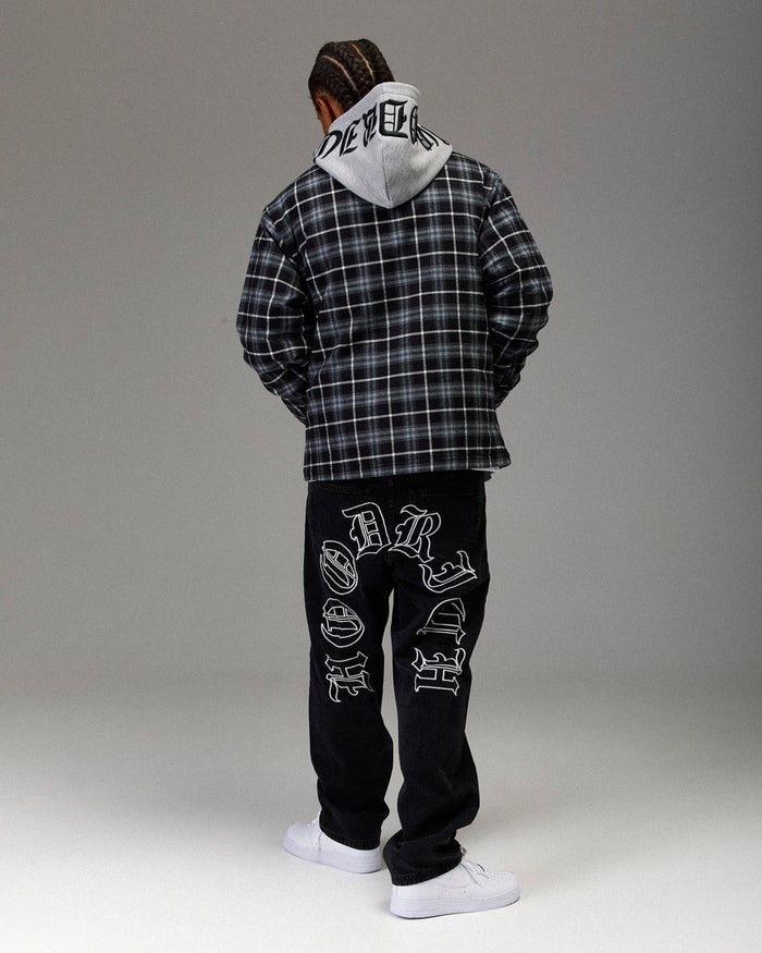 Person wearing a plaid jacket and black pants with white text, standing against a gray background